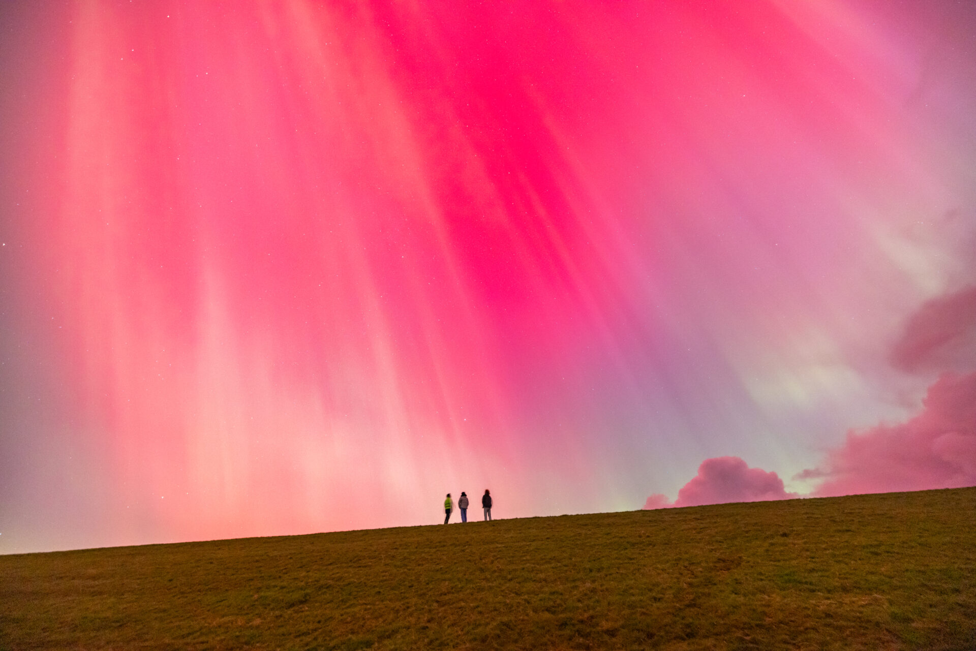 Drie mensen op een dijk onder roze noorderlicht